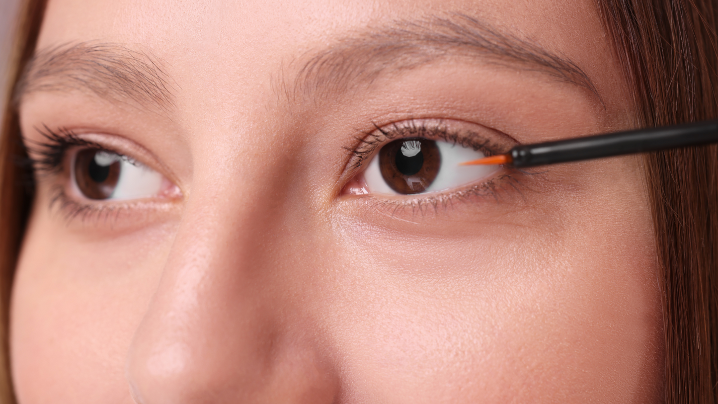 Woman applying Luna Nectar Moon Boost lash serum to her upper lash line with a thin applicator brush.