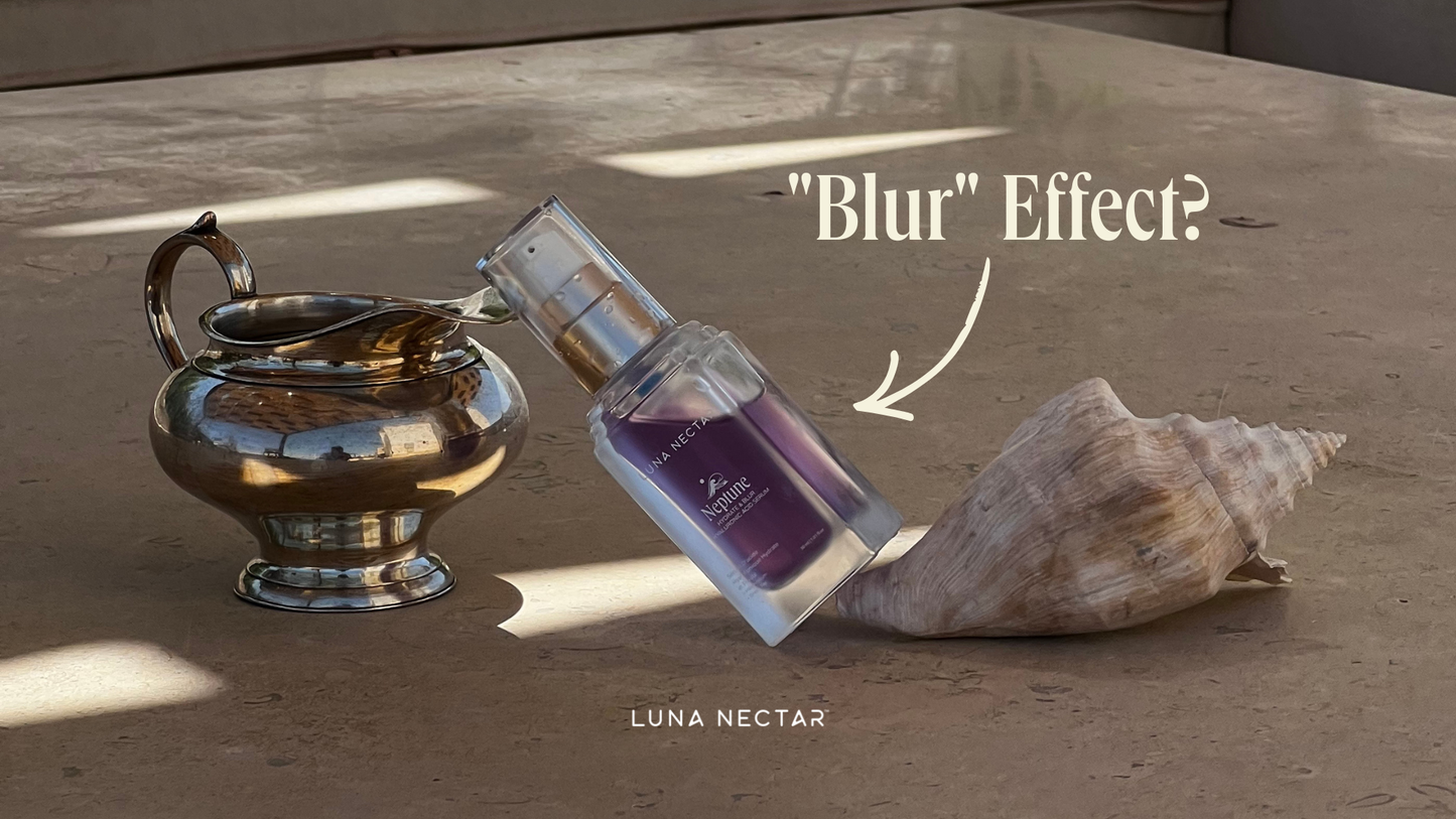 Bottle of Luna Nectar Neptune Hydrate & Blur Serum leaning against a seashell beside a reflective silver vessel on a stone surface, with the text “Blur Effect?” displayed above.